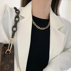 Detail of gold snake chain necklace with geometric links on model in white blazer