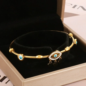 Detail view of gold Evil Eye bangle with blue zircon and heart charm on black velvet