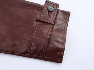 Detailed close-up of reddish-brown leather jacket cuff with decorative strap and button