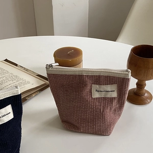 Pink corduroy makeup pouch with a vintage label shown in a cozy lifestyle setting