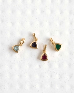 Detailed view of four golden triangle pendants with colorful zircon birthstones on a white surface