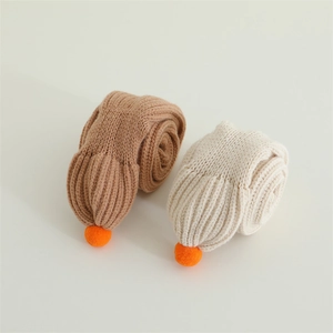 Detailed texture of thick knit baby scarves with orange pom-poms in camel and cream