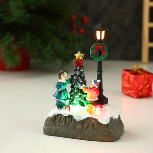 Luminous Christmas miniature with figures decorating a tree near a glowing street lamp