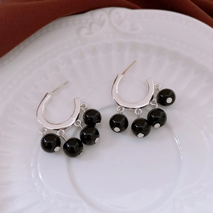 Detailed close-up of C-shaped silver earrings with three black beads on a white ceramic plate