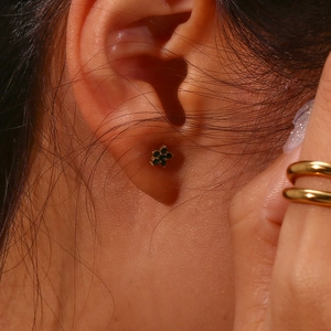 Gros plan d'un clou d'oreille fleur dorée avec zircons verts porté à l'oreille