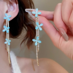 Detail shot of blue resin flower earrings with long crystal tassel chains on model
