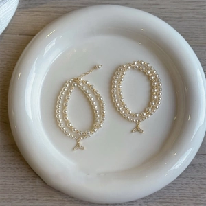 Double-layered pearl bracelet with a golden zircon fishtail pendant on white plate