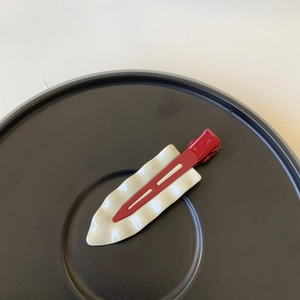 Close-up of a red and white wavy leaf hair clip on a minimalist black display plate