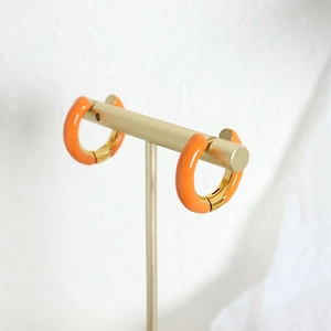 Modern orange enamel C-shaped hoop earrings on a minimalist gold display stand