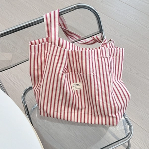 Detail of red and white striped canvas tote bag resting on a modern chair in a sunny setting