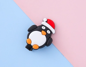 Détail de la barrette pingouin de Noël avec bonnet rouge sur fond bleu et rose