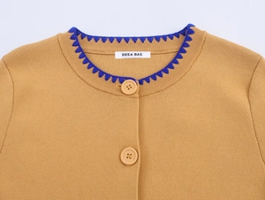 Detail of camel knit cardigan showing blue scalloped trim and buttoned crew neck