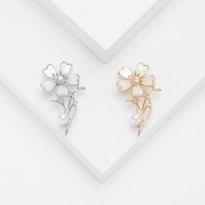 Elegant gold and silver flower brooches with pearls and crystals on a white pedestal