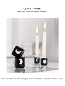 Close-up of black ceramic candle holder with white moon pattern and warm candle flame