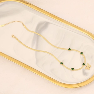 Gold emerald heart necklace with butterfly pendant on marble tray, 18K plated snake chain