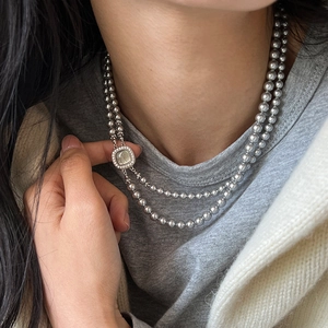 Close-up of a double-layer pearl necklace featuring a vintage square gemstone pendant
