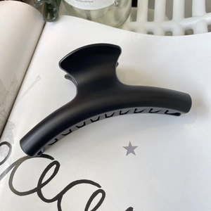Close-up of a large matte black shark hair clip on a minimalist magazine background