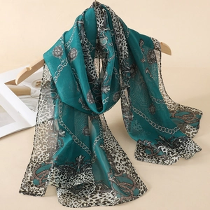 Detail of teal chiffon scarf with leopard print and chain patterns on a wooden hanger