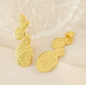Macro shot of 18K gold plated lava style earrings with hammered texture on silk