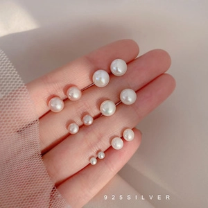Macro detail of various sizes of S925 silver pearl earrings displayed on fingers