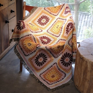 Detail of bohemian woven picnic blanket with vintage orange floral pattern and tassels