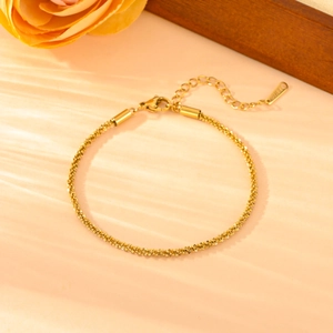 Minimalist gold twisted chain bracelet with adjustable extender on a warm floral background