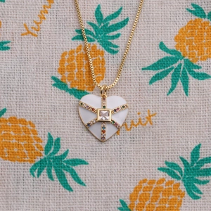 Détail du pendentif cœur blanc avec zircons colorés et chaîne dorée sur tissu
