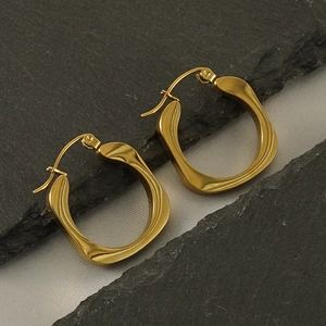 Close-up of 18k gold plated square stud earrings on dark rock and white silk