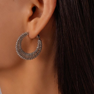 Close-up of textured silver hoop earring with geometric relief design on model's ear