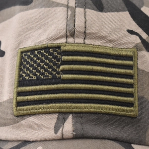 Close-up of tactical US flag embroidery on a camo canvas baseball cap surface