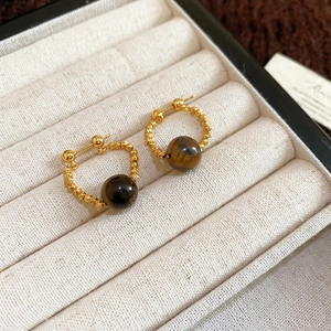 Dettaglio di orecchini a tortiglione in oro 18k con perle di pietra occhio di tigre