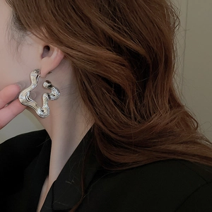 Close-up of irregular silver wave earrings worn by a model for a high-end metallic look