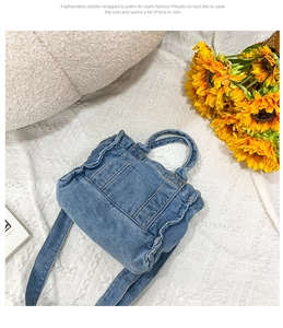 Top view of blue denim handbag with ruffle edges and straps on white textured background