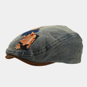 Close-up of retro washed denim beret with distressed orange patch and brown brim.