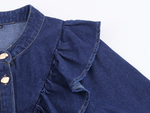Détail de chemise en jean bleu foncé avec volants superposés et boutons dorés