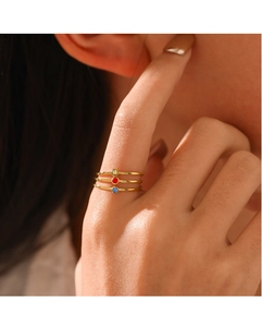 Close-up of three stacked gold-plated steel rings featuring red, blue, and yellow gemstones