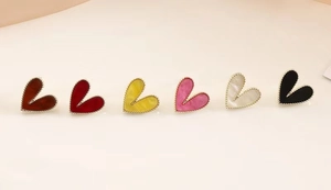 Flat lay of small heart-shaped stud earrings in six vibrant colors with gold metal borders