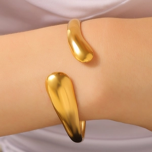 Close-up of a gold-plated fluid geometry open bangle with a polished mirror finish