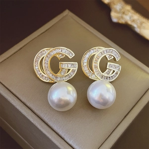 Elegant gold double-G letter earrings with zircon and pearls in a 45-degree macro view