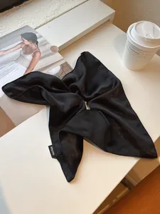 Detail of a shiny black satin hair scrunchie with a handmade woven label and smooth texture
