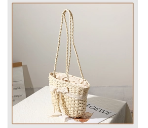 Detail of handmade straw tote bag featuring white lace trim and bow on desktop