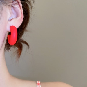 Detailed view of matte red C-shaped acrylic earrings worn with a minimalist fashion style