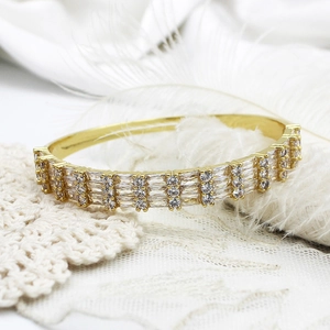 Close-up of gold geometric devil eye bangle with pave-set zircon on white lace background