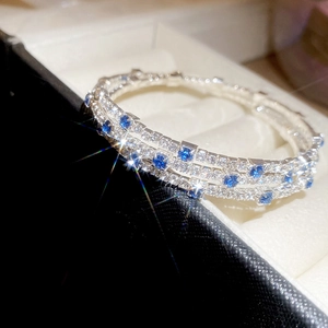 Macro detail of a triple-layer silver bangle with cubic zirconia and blue square gemstones