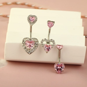 Three silver navel rings with pink heart zircons on white display stand