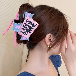 Detail of denim bow hair claw with pink 'THIS IS ME' embroidery on side of hair accessory