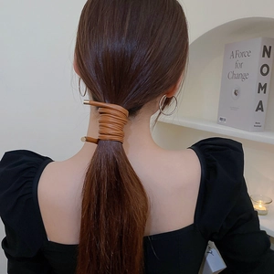 Detail of dark brown leather hair tie with gold metal tips wrapped on a ponytail