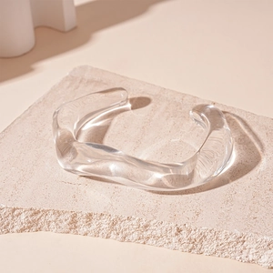 Detailed view of a transparent wavy acrylic bangle placed on a beige textured stone