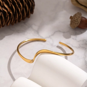 Minimalist 18K gold plated stainless steel wave open cuff bracelet on stone pedestal