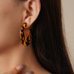 Detail of round tortoiseshell resin earrings showing leopard texture on female model